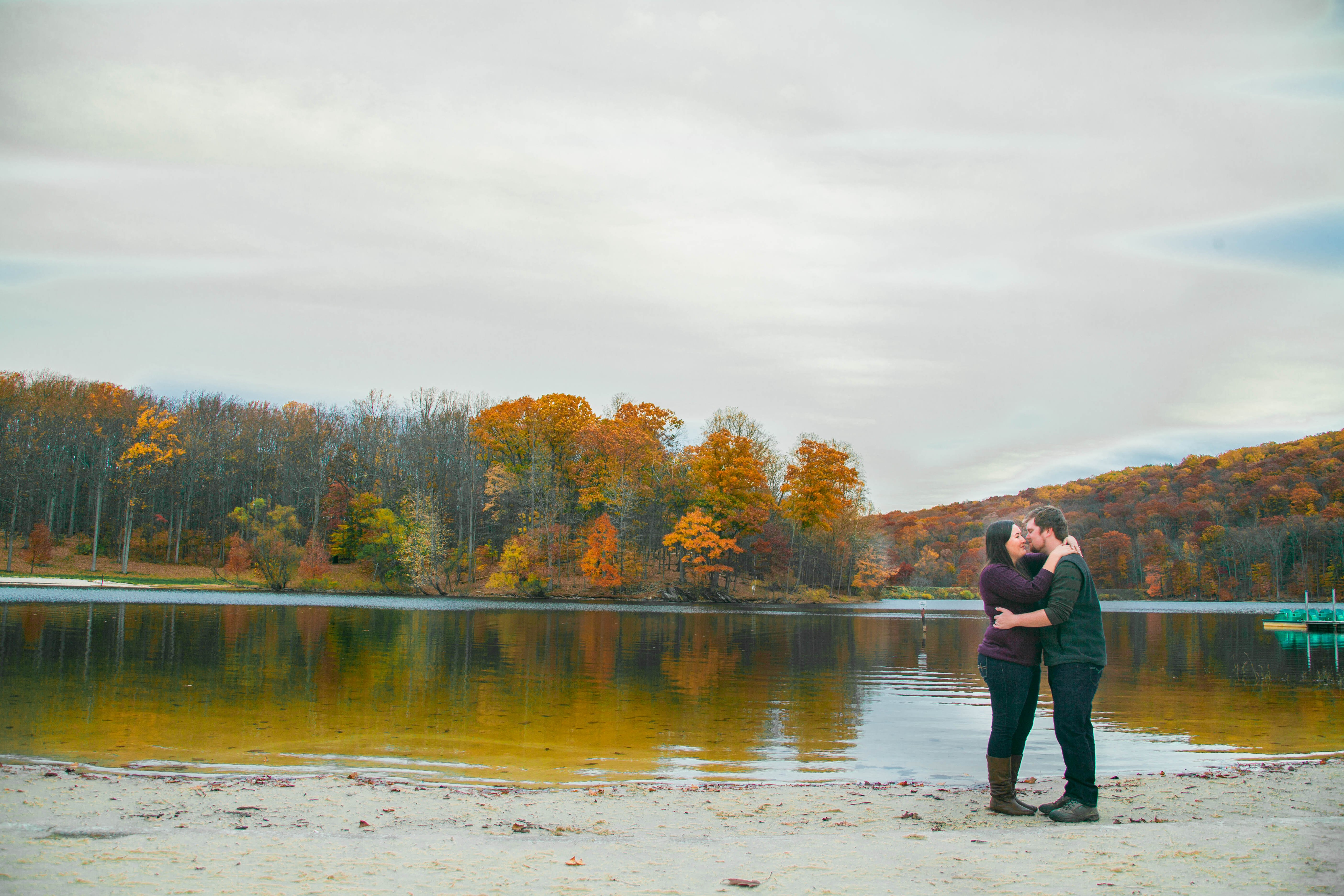 a couple stands in each others embrace infront of lake cunningham in the fall