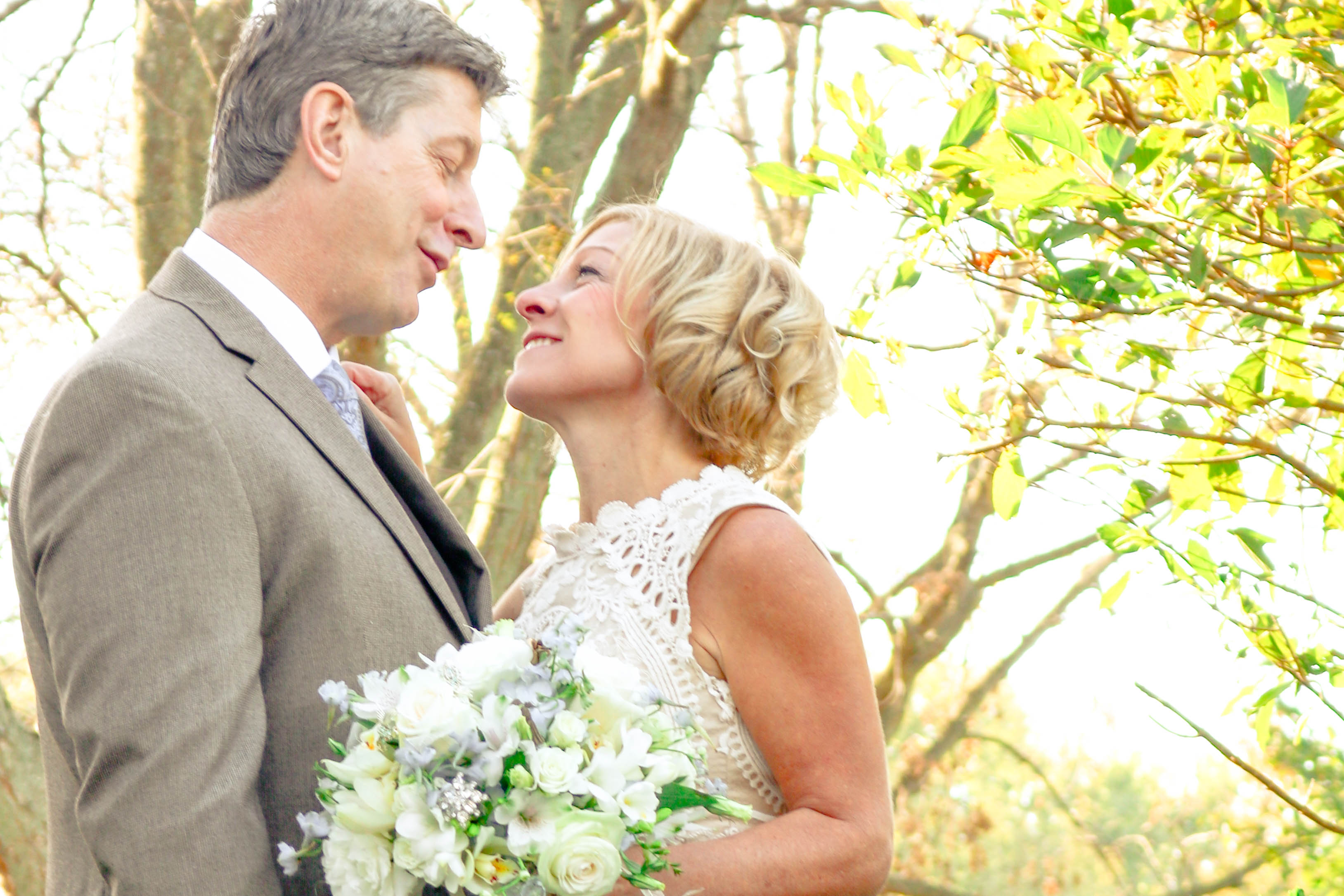 A bride and groom stand close surrounded by fall leaves