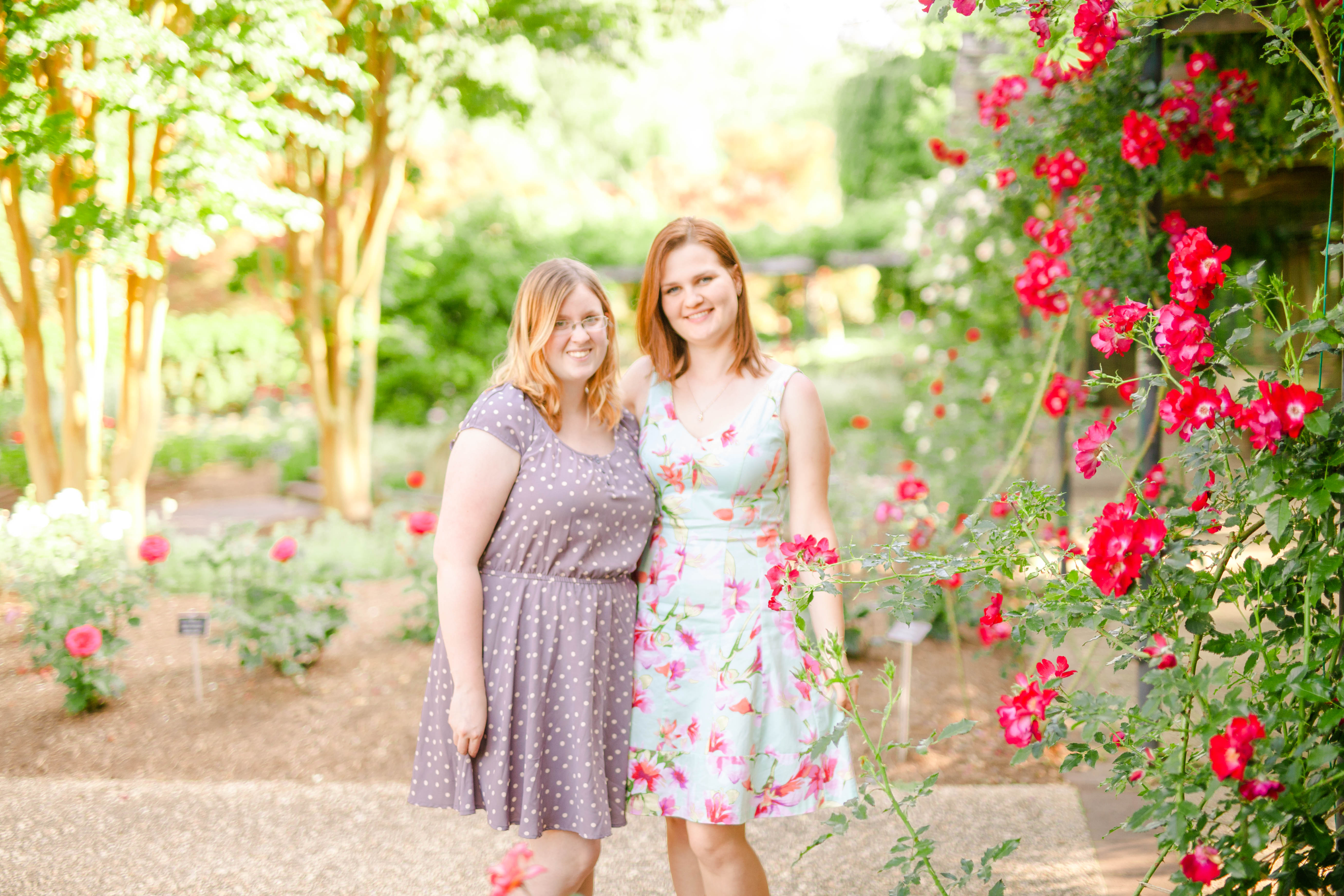 Two best friends in dresses standing in a rose garden