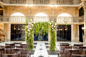 A styled floral backdrop sits at the back of a Ceremony inside the George Peabody Library in Baltimore, MD