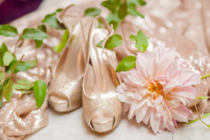 A glittery pair of peep toe pumps is styled with pink flowers, greenery and sparkly fabric for an inspiration shoot at the George Peabody Library in Baltimore, MD