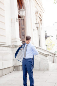A groom stands outside the George Peabody Library in Baltimore MD putting on a navy blue suit jacket