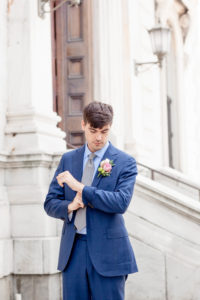 A groom stands outside the George Peabody Library in Baltimore MD adjusting the cuffs of his royal blue navy suit