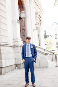 A groom stands outside the George Peabody Library in Baltimore MD wearing a royal blue suit