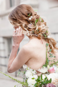 A bride stands outside the George Peabody Library in Baltimore, MD adjusting her earring and showing off her floral inspired hair style