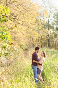 A September backyard anniversary session in Woodsboro MD. A couple stands together looking at each other lovingly in the tall grass under the glowy sun
