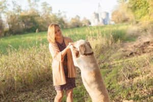 A September backyard anniversary session in Woodsboro MD. A girl dances with her dog in a field smiling and laughing