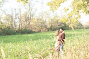A September backyard anniversary session in Woodsboro MD. A wife leaps into her husbands arms in the tall grass under the glowing sun
