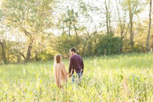 A September backyard anniversary session in Woodsboro MD. A couple stands in a loving embrace under the golden glow of the sun facing the wide expanse of trees