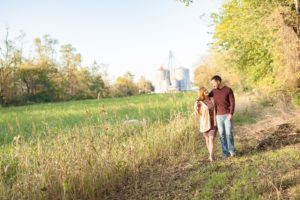 A September backyard anniversary session in Woodsboro MD. A couple walks together, looking at each other lovingly, beside a field of tall grass