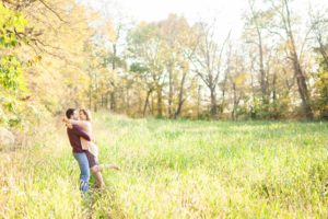 A September backyard anniversary session in Woodsboro MD. A wife leaps into her husbands arms in the tall grass under the glowing sun