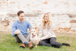 Cozy Autumn Engagement Session at Rockburn Branch Park in Elkridge, MD. A couple sits in front of a brick building with their dog 