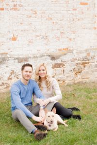 Cozy Autumn Engagement Session at Rockburn Branch Park in Elkridge, MD. A couple and their dog sit snuggled up in front of a brick building for a fall photo session