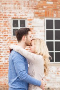 Cozy Autumn Engagement Session at Rockburn Branch Park in Elkridge, MD. A loving couple stands in front of a brick building embracing