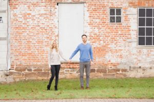 Cozy Autumn Engagement Session at Rockburn Branch Park in Elkridge, MD. A couple stands in front of a brick building holding hands
