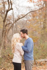 Cozy Autumn Engagement Session at Rockburn Branch Park in Elkridge, MD. A loving couple embraces in a park surrounded by fall trees, and nuzzles noses