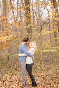 Cozy Autumn Engagement Session at Rockburn Branch Park in Elkridge, MD. A loving couple embraces in a park surrounded by fall trees, and laughs together