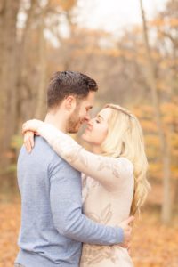 Cozy Autumn Engagement Session at Rockburn Branch Park in Elkridge, MD. A loving couple stands in sweet embrace with golden fall leaves in the background