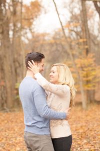 Cozy Autumn Engagement Session at Rockburn Branch Park in Elkridge, MD. A loving couple stands in an joyful embrace with golden fall leaves in the background