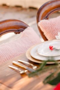 pink fluffy pillows sit on chairs tucked into a sweetheart table with gold dinnerware for a Christmas Wedding at the Liriodendron Mansion in Bel Air Maryland