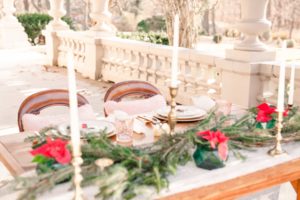 A sweetheart table for a Christmas winter wedding with a table draped in lace and evergreens. Dotted with candles and poinsettias this table sits on the back porch of the Liriodendron Mansion in Bel Air Maryland 