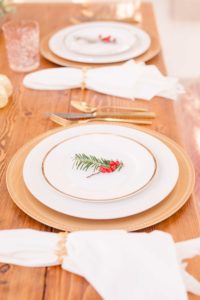 A sweetheart table for a Christmas winter wedding with a gold plated table setting, gold wrapped napkins, and a spring of holy sitting on the top gold rimmed plate on the back porch of the Liriodendron Mansion in Bel Air Maryland 
