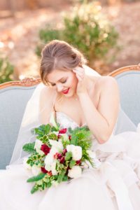 A young bride sits on a chaise lounge holding a holiday bouquet created by Fleur De Charme at the Liriodendron Mansion in Bel Air Maryland for her winter wedding