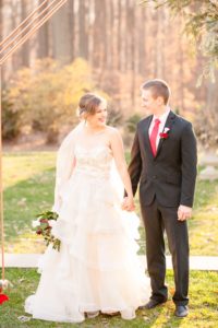 A young bride and groom smile at each other under a Holiday themed ceremony arch at the Liriodendron Mansion in Bel Air Maryland for her winter wedding