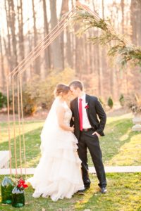 A young bride and groom share a quiet moment under a Christmas themed ceremony arch at the Liriodendron Mansion in Bel Air Maryland for their winter wedding