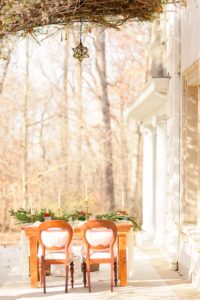 A sweetheart table for a Christmas winter wedding with a table draped in lace and evergreens. Dotted with candles and poinsettias this table sits on the back porch of the Liriodendron Mansion in Bel Air Maryland 