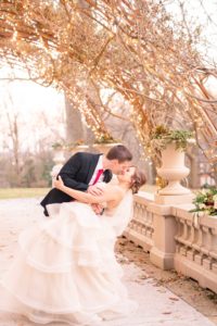 A young groom dips his bride down low for a kiss under the twinkle lights on the back porch of the Liriodendron Mansion in Bel Air Maryland for a Christmas Winter Wedding