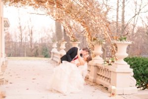 A young groom dips his bride down low for a kiss under the twinkle lights on the back porch of the Liriodendron Mansion in Bel Air Maryland for a Christmas Winter Wedding