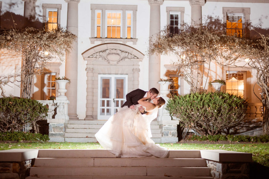A groom dips his bride in front of the Liriodendron Mansion in Bel Air Maryland at a winter wedding for a night portrait