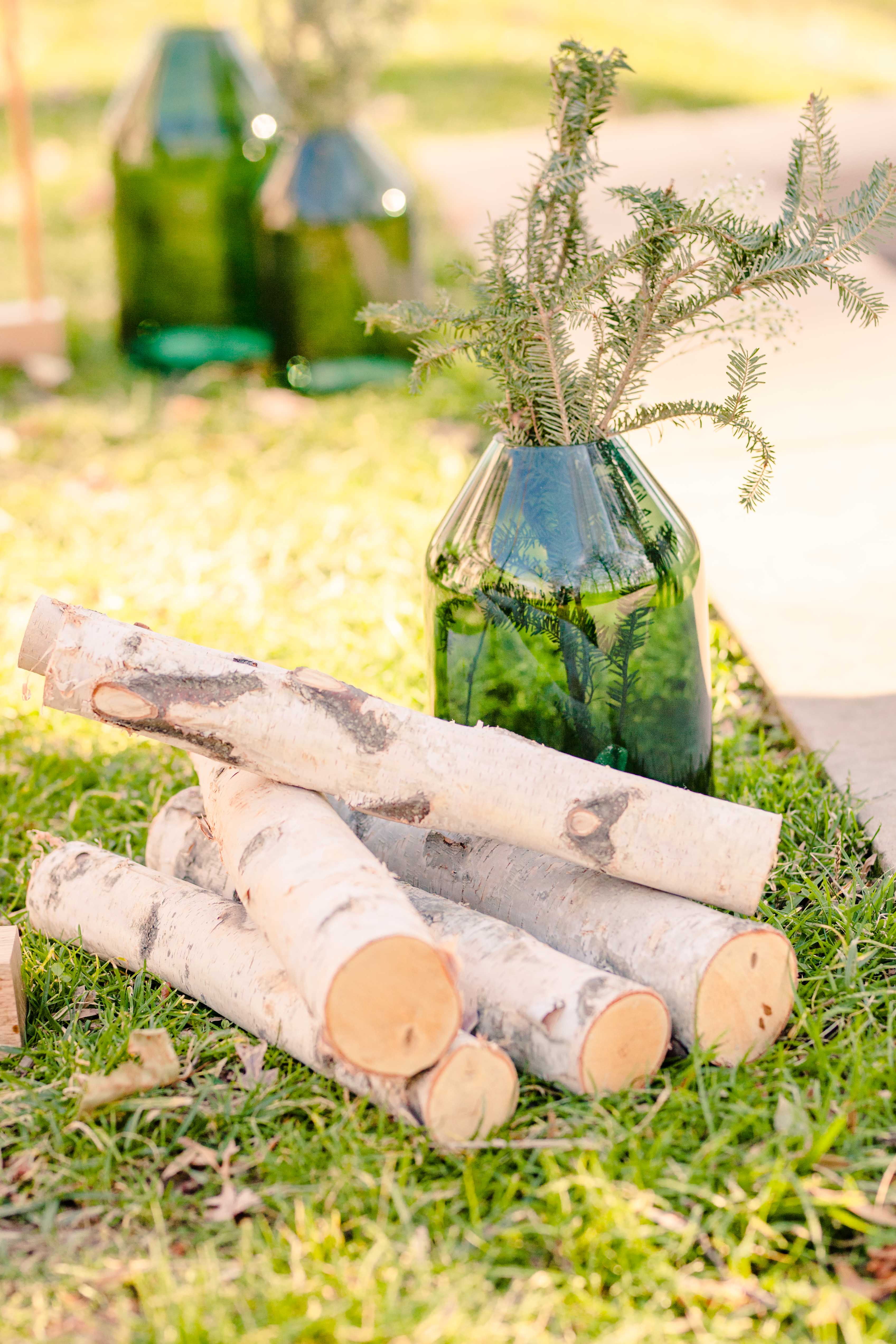 A pile of logs rest next to a green jar of greenery in front of a wedding arch for a styled shoot styled by Atwater Lane