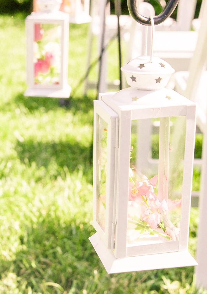 Ceremony details of a white lantern hanging next to each row down the aisle with pink flowers inside in a summer garden wedding Airlie in Warrenton Virginia