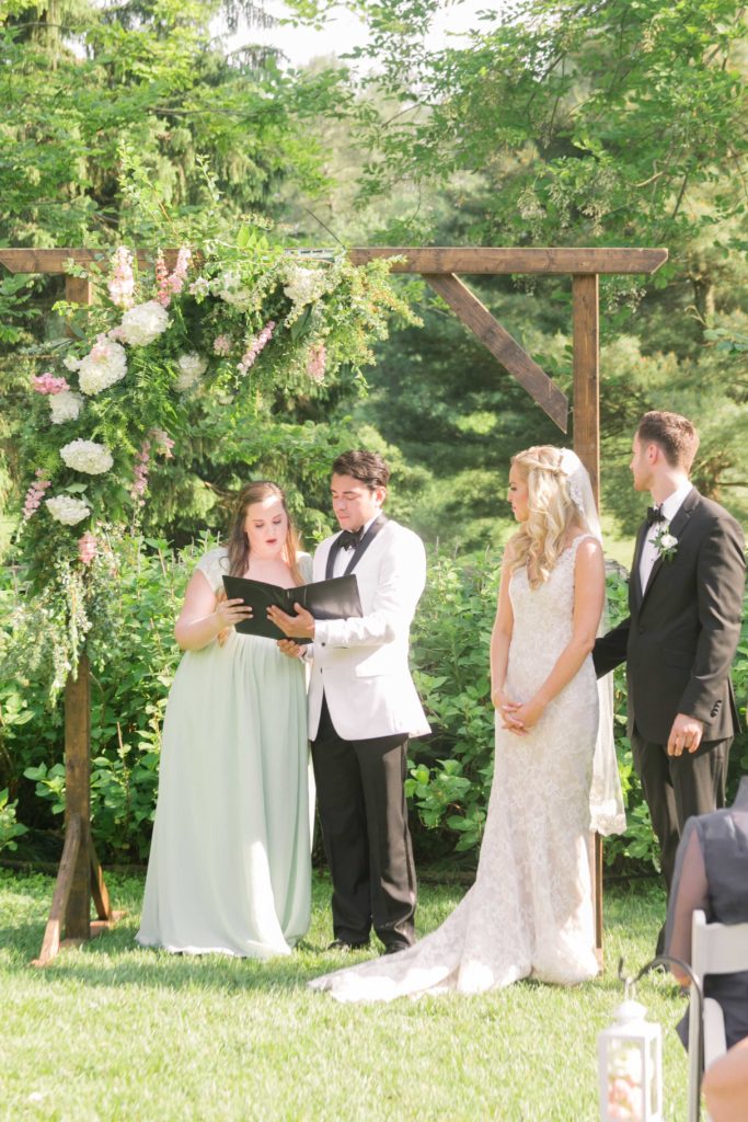 Maid of honor reads a poem underneath a flowering arch making their vows in a summer garden wedding Airlie in Warrenton Virginia