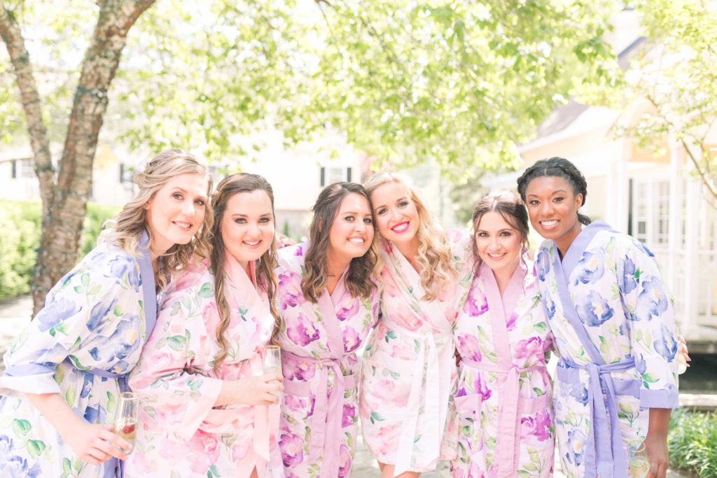 Bride and Bridesmaids toast outside in the gardens in floral robes at a summer garden wedding Airlie in Warrenton Virginia