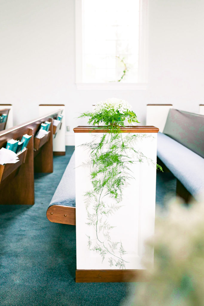 Gold wreaths lined with greenery and white flowers line the aisle with greenery cascading down the sides as ceremony details for a summer frederick maryland wedding at the Seventh Day Adventist Church