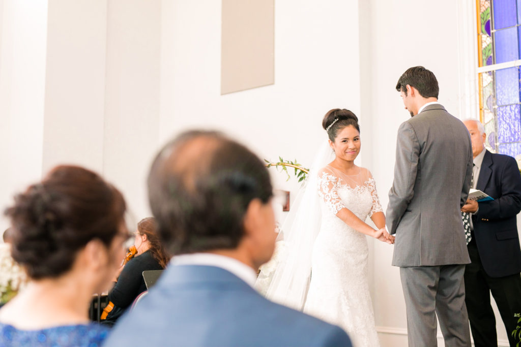 The bride glances over at her parents while holding hands with her groom in a latino wedding in the summer in frederick maryland wedding at the Seventh Day Adventist Church