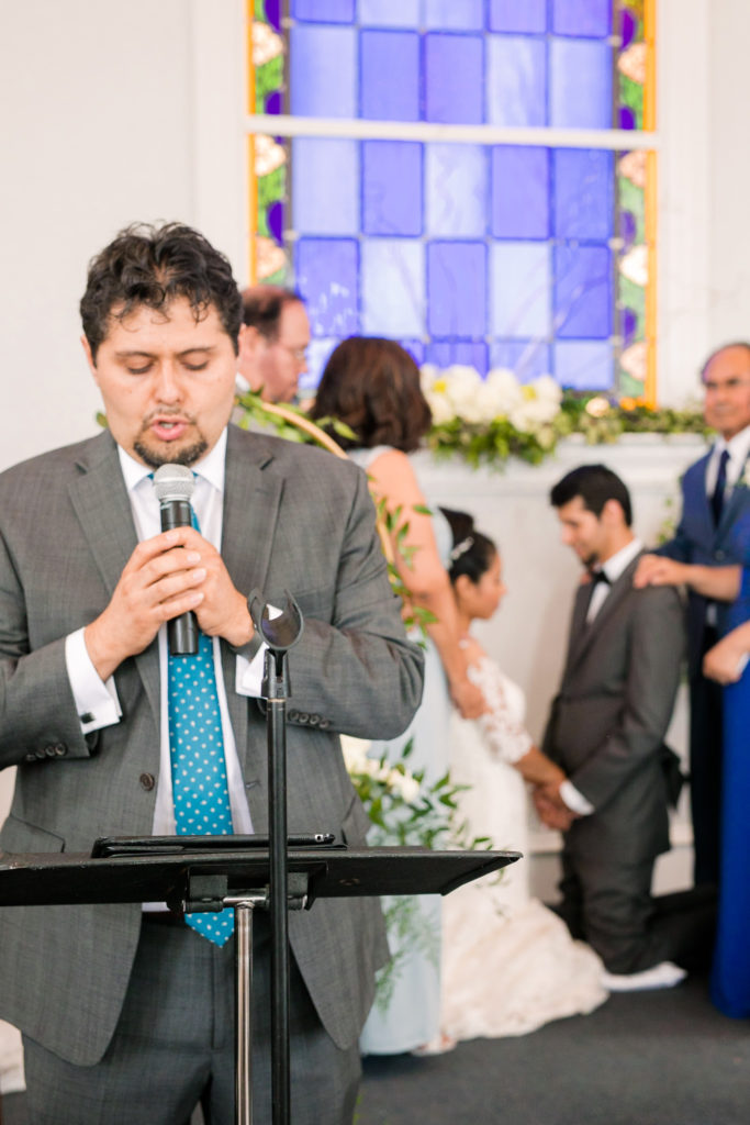 the Bride and groom kneel together in prayer with their parents standing over them while a soloist sings a song in a latino wedding in the summer in frederick maryland wedding at the Seventh Day Adventist Church