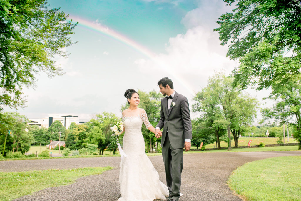 Summer Frederick Maryland Wedding at Prospect Hall Mansion with a joyful couple walking in front of a rainbow