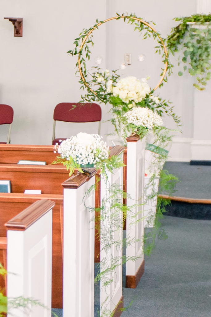Gold wreaths lined with greenery and white flowers line the aisle as ceremony details for a summer frederick maryland wedding at the Seventh Day Adventist Church