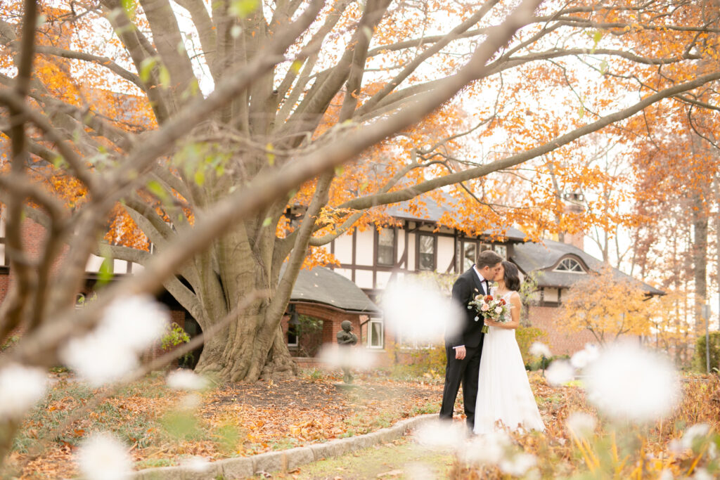 A bride and groom share a kiss in front of the Gramercy Mansion in the fall for Maryland Wedding Photographer